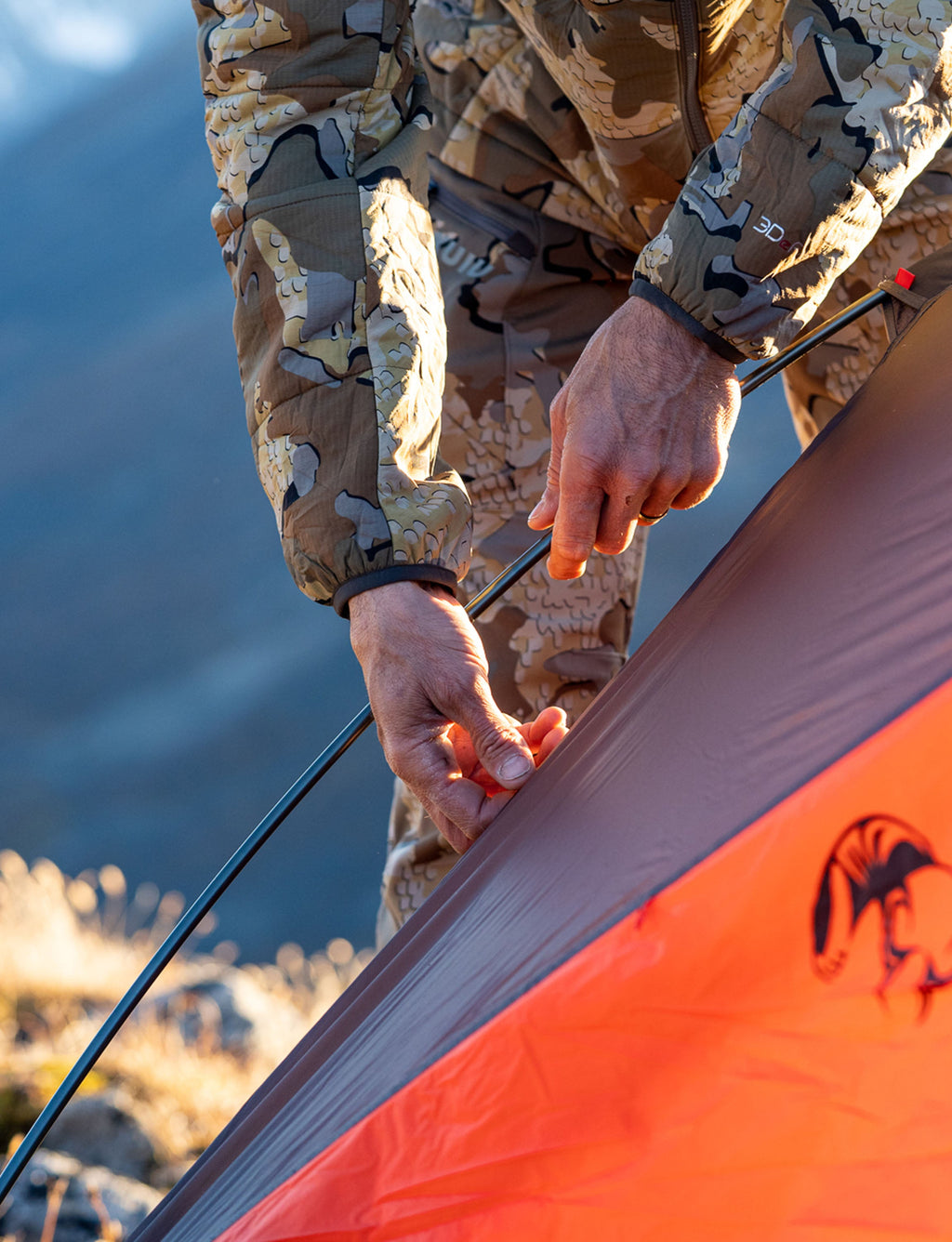Close-up Hunter attaching tent pole to the Mountain Star 2 Person Tent in Gunmetal Grey, Orange