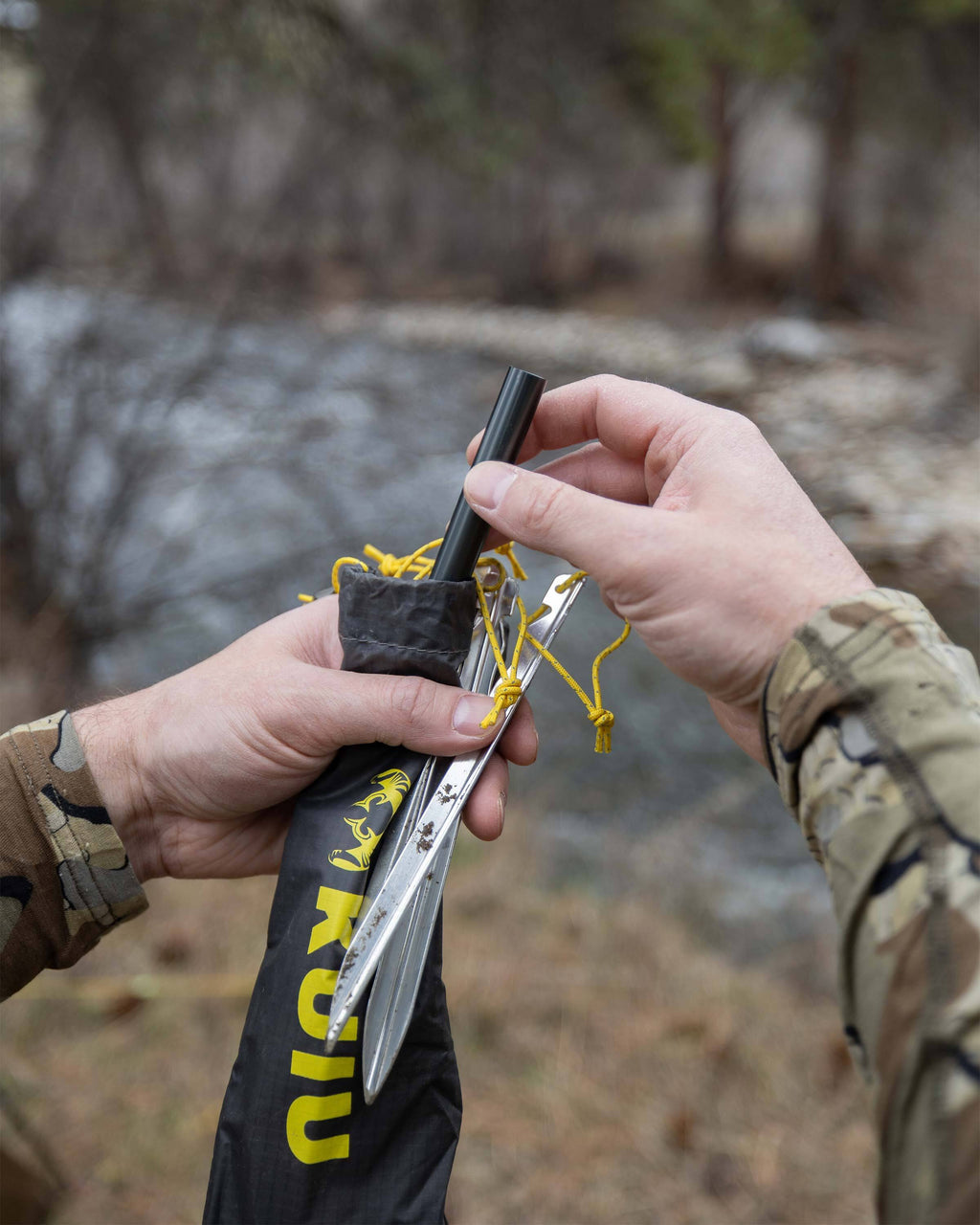 Detailed close up of hunter removing the emergency pole repair splint and silver colored V-stakes from the stake bag for his Mountain Star 3 Person Tent