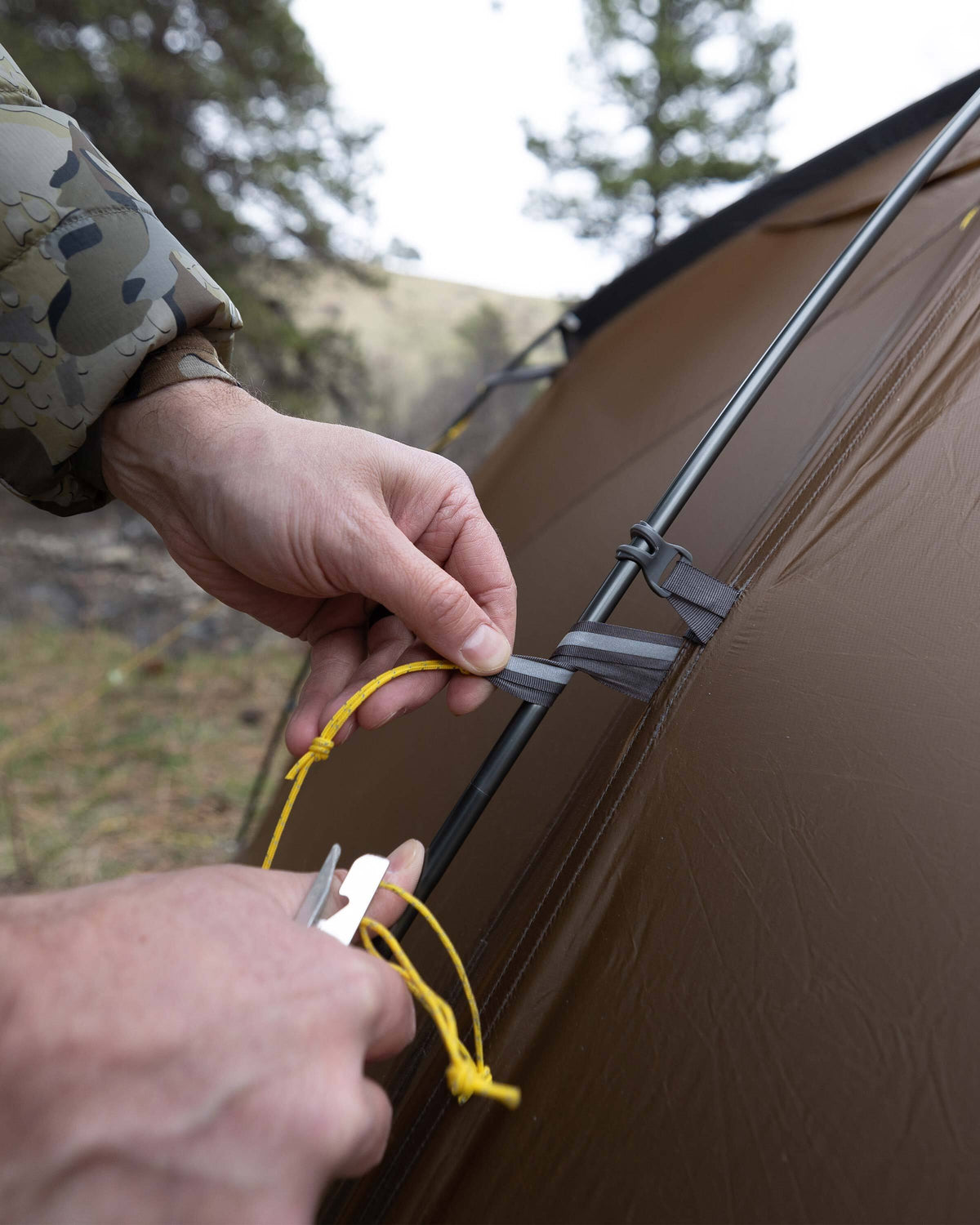 Detailed close up image showing the hunter properly wrapping the guy lines around the aluminum pole structure of the Mountain Star 3 Person Tent for additional support