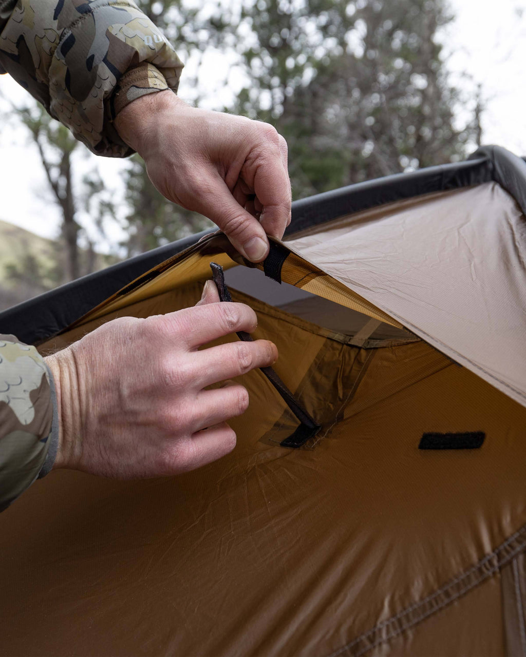Detailed close up image showing the hunter opening the rain fly vent of the Mountain Star 3 Person Tent in Camel Brown for additional air flow and ventillation