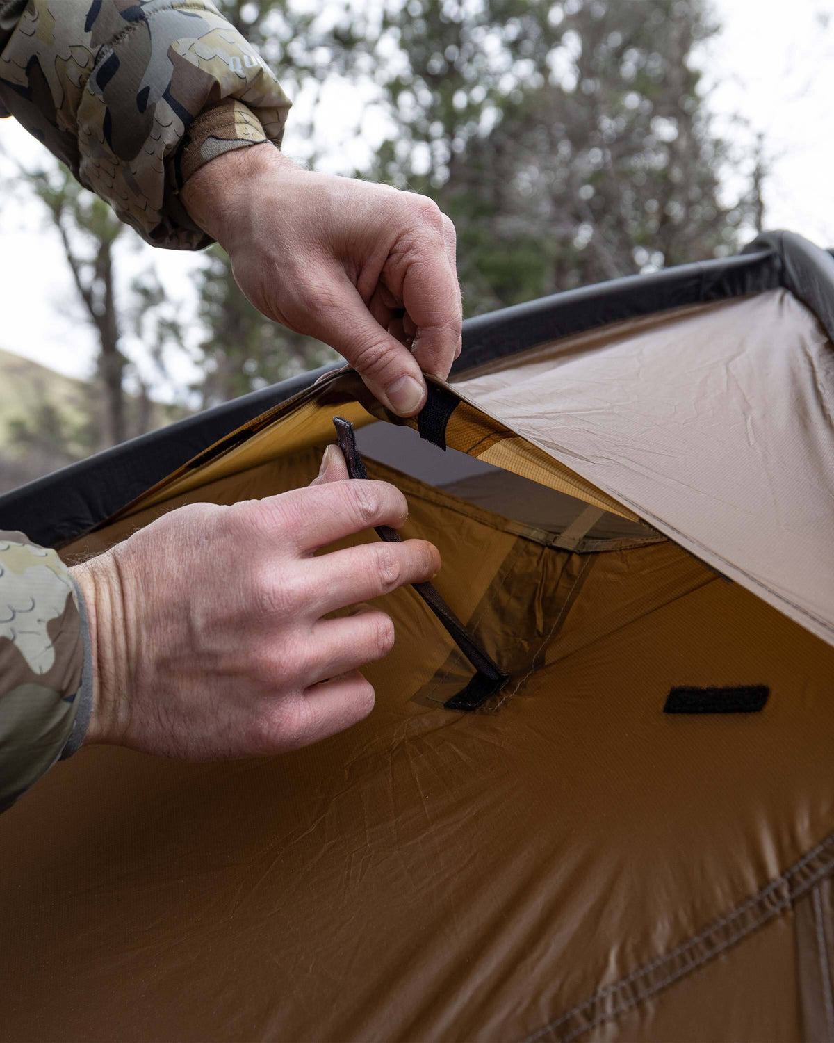 Detailed close up image showing the hunter opening the rain fly vent of the Mountain Star 3 Person Tent in Camel Brown for additional air flow and ventillation