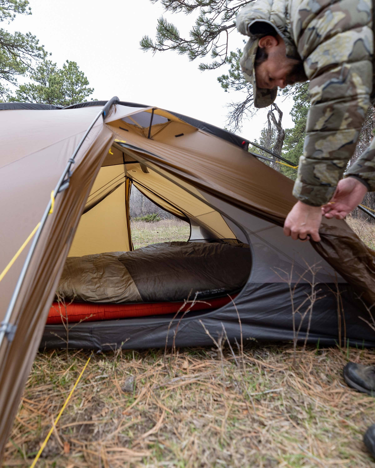Hunter rolling up the vestibule door of the Mountain Star 3 Person Tent in Camel Brown to show through the interior of the tent through both open vestibule doors