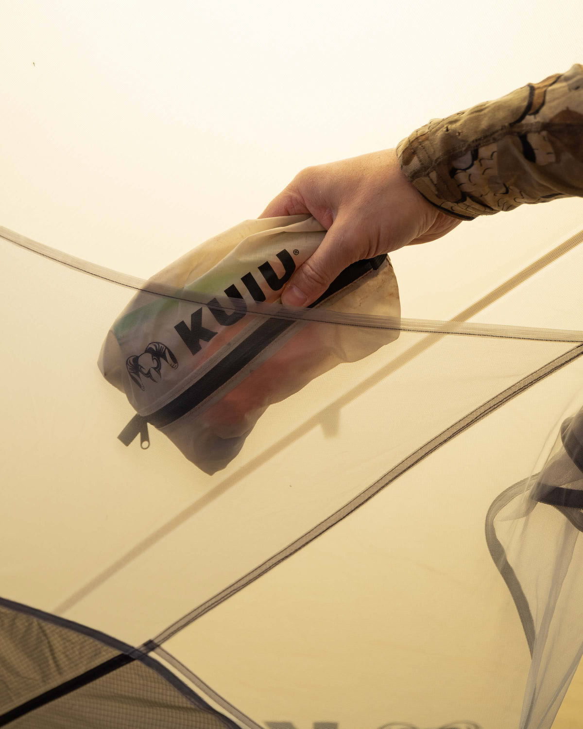 Hunter stashing clear zip dry bag inside of integrated cargo stash pockets sewn into the mesh body of the Mountain Star 3 Person Tent