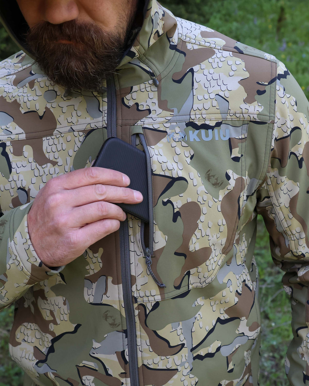 Close-up of hunter putting a cell phone in the front zippered pocket of the Alpine Hooded Jacket in Valo Camouflage