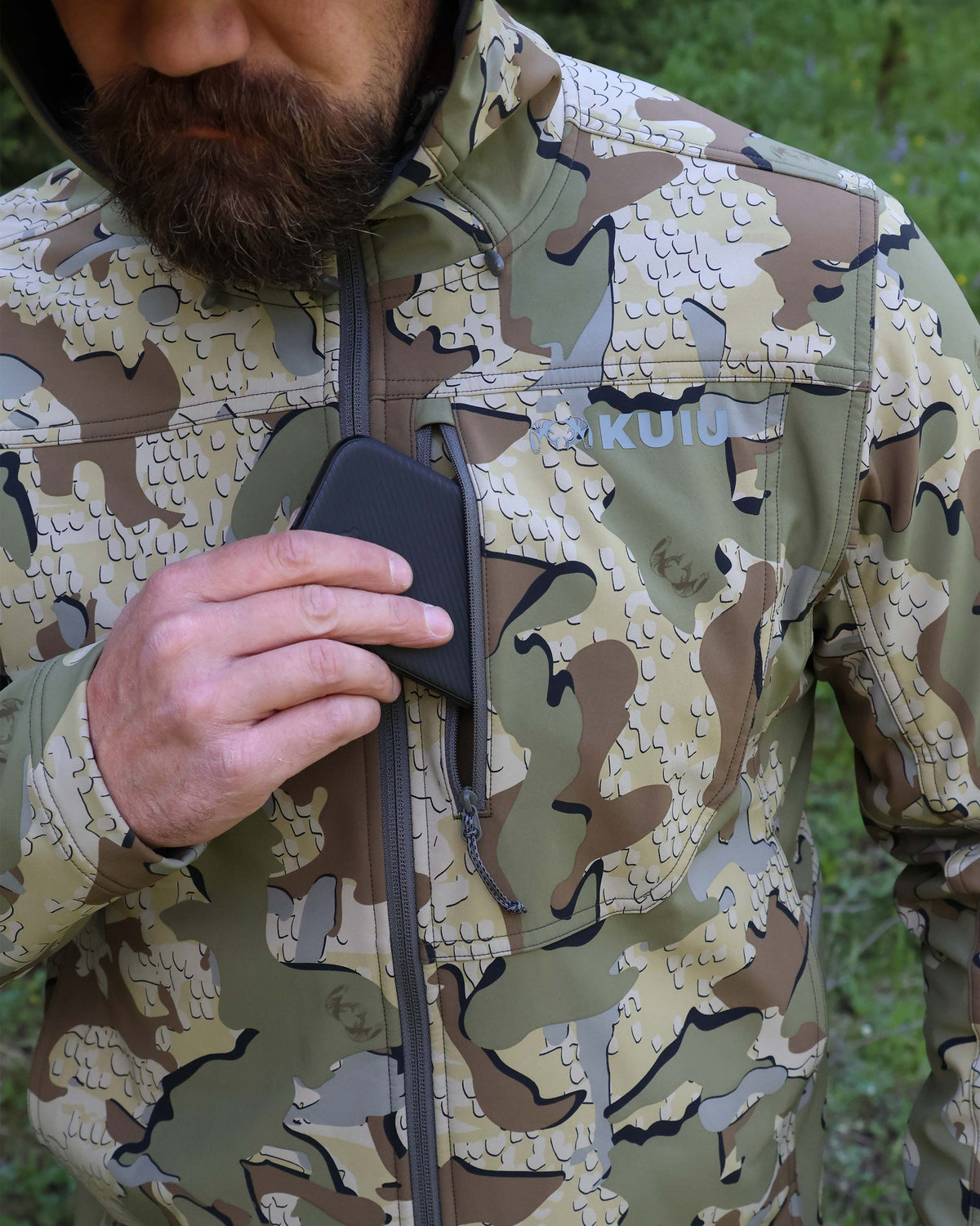 Close-up of hunter putting a cell phone in the front zippered pocket of the Alpine Hooded Jacket in Valo Camouflage