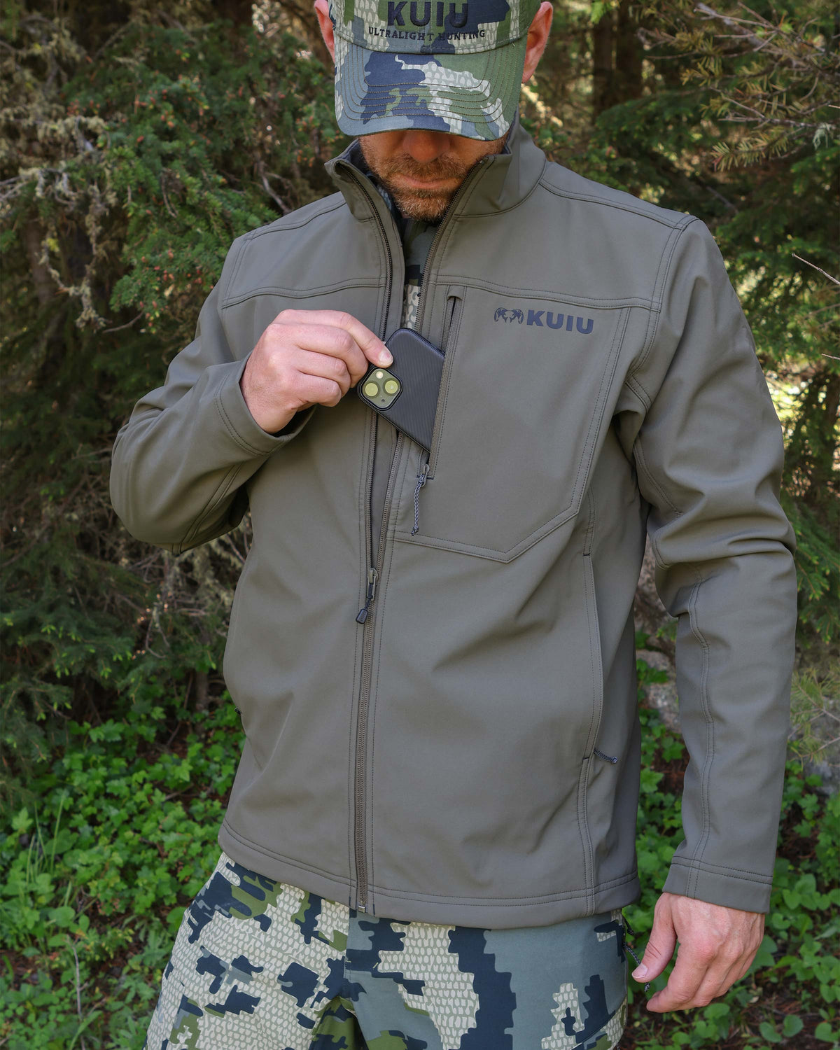 Front of hunter putting a cell phone in the front left chest pocket of the Alpine Jacket in Ash Brown