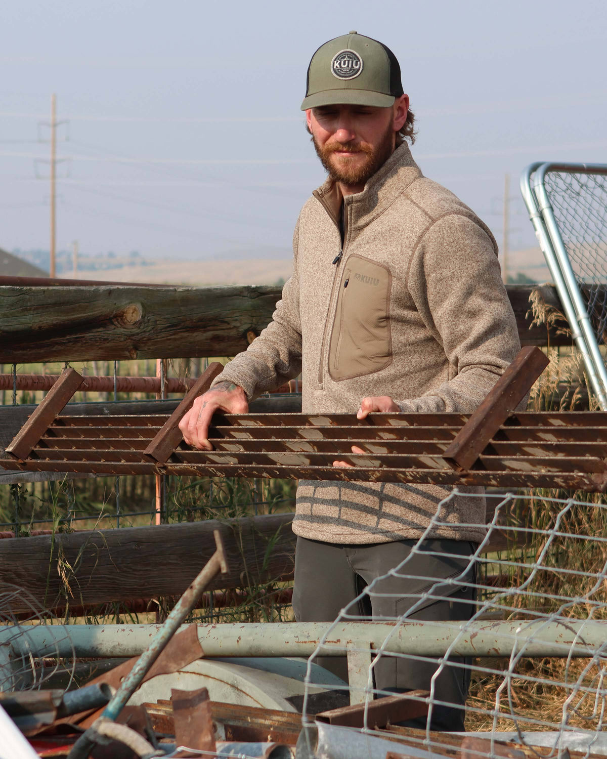 Man piling metal scraps together, wearing Base Camp Pullover Sweater in Khaki Heather 