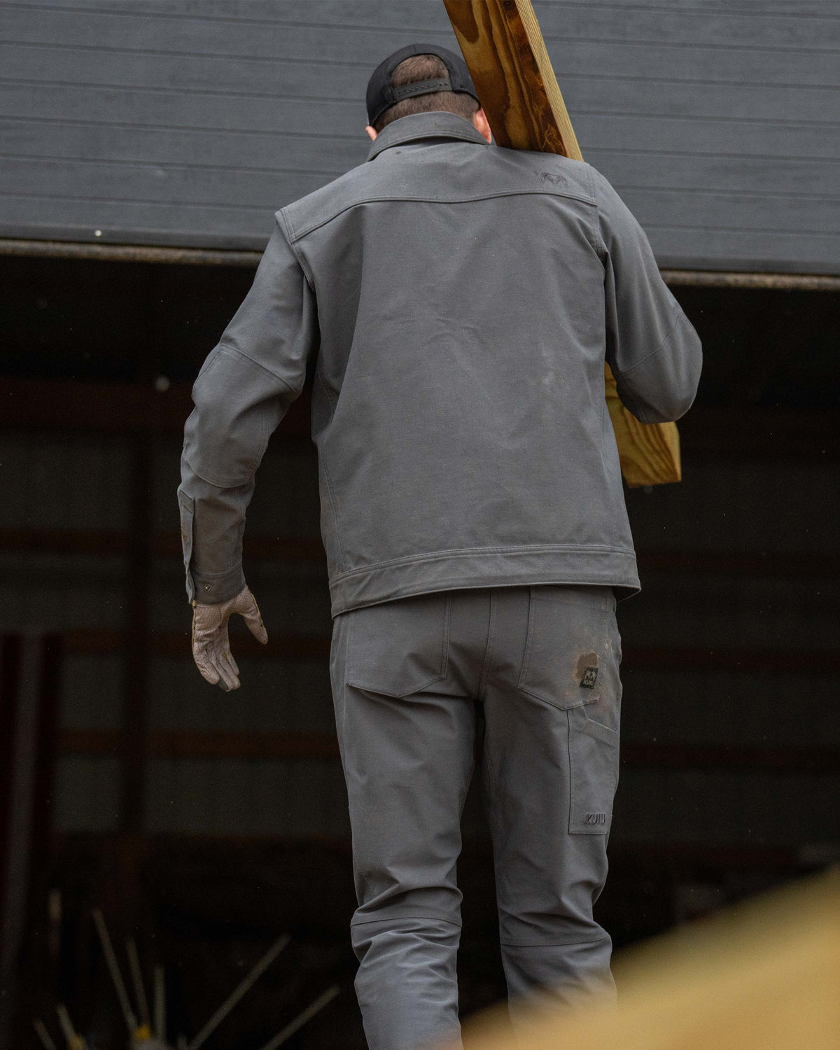 Back view of man carry a wood stud on his shoulder, wearing Brawley Pant in Gunmetal Grey