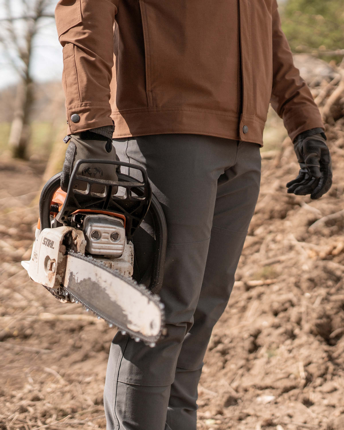 Man carrying a chainsaw, a close view highlighting the fit of Brawley Pant in Gunmetal Grey
