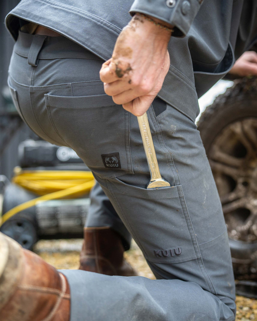 Close-up, back view of man kneeling down, putting a wrench in his back pocket, wearing Brawley Pant in Gunmetal Grey 