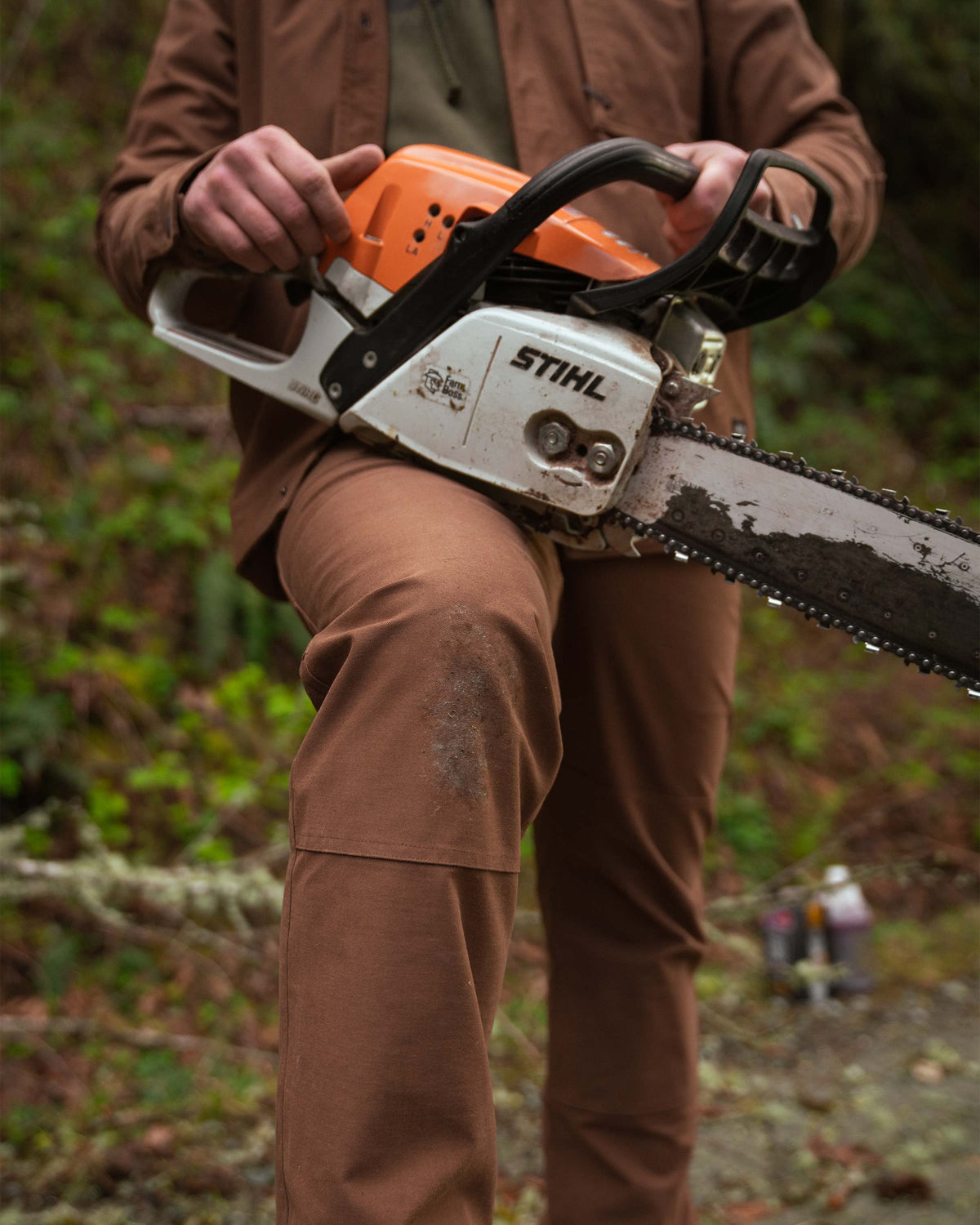Front view of man propping a chainsaw on his leg, highlighting the double panel overlay on the knees on Brawley Pant in Saddle Brown
