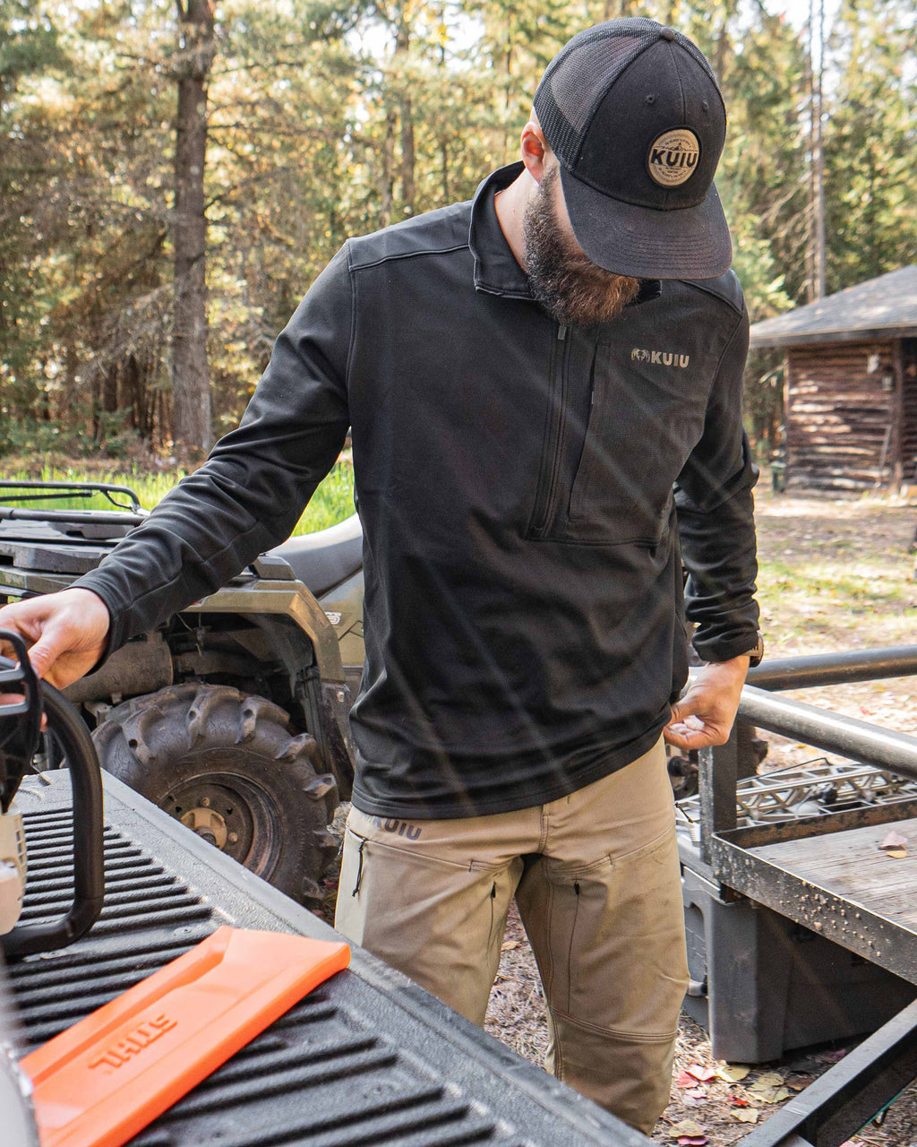 Hunter stands near an ATV and behind pickup truck tailgate, in a wooded area, wearing Bicomp Zip-T in Black