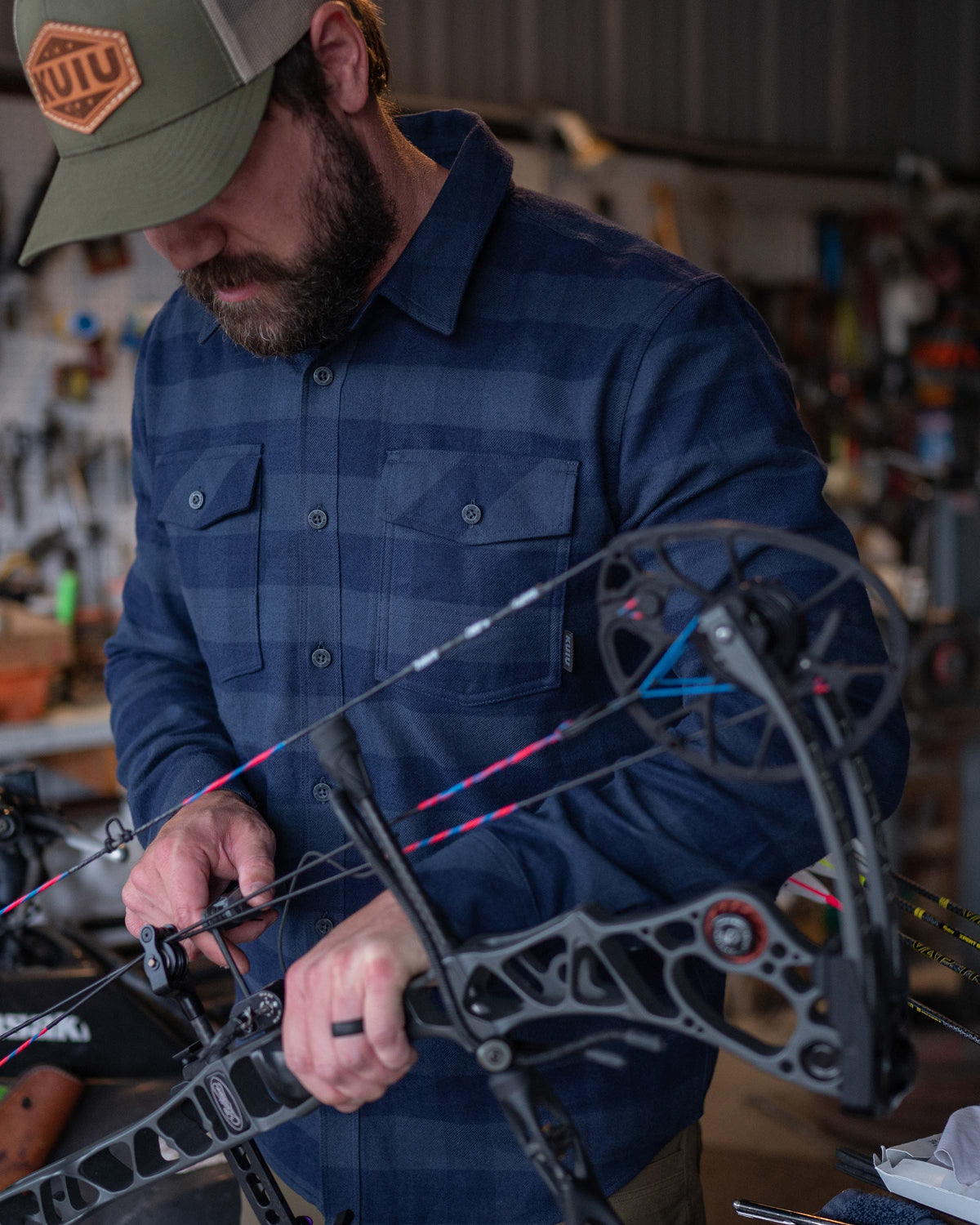 Man adjusting compound bow wearing Field Flannel Shirt in Steel Blue Buffalo Check