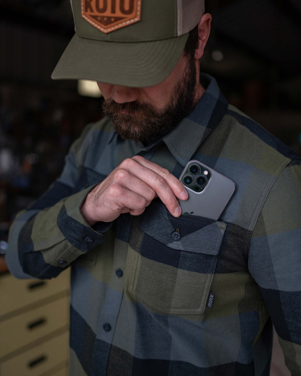 Phone being placed in chest pocket of Field Flannel Shirt in Verde Camouflage Plaid
