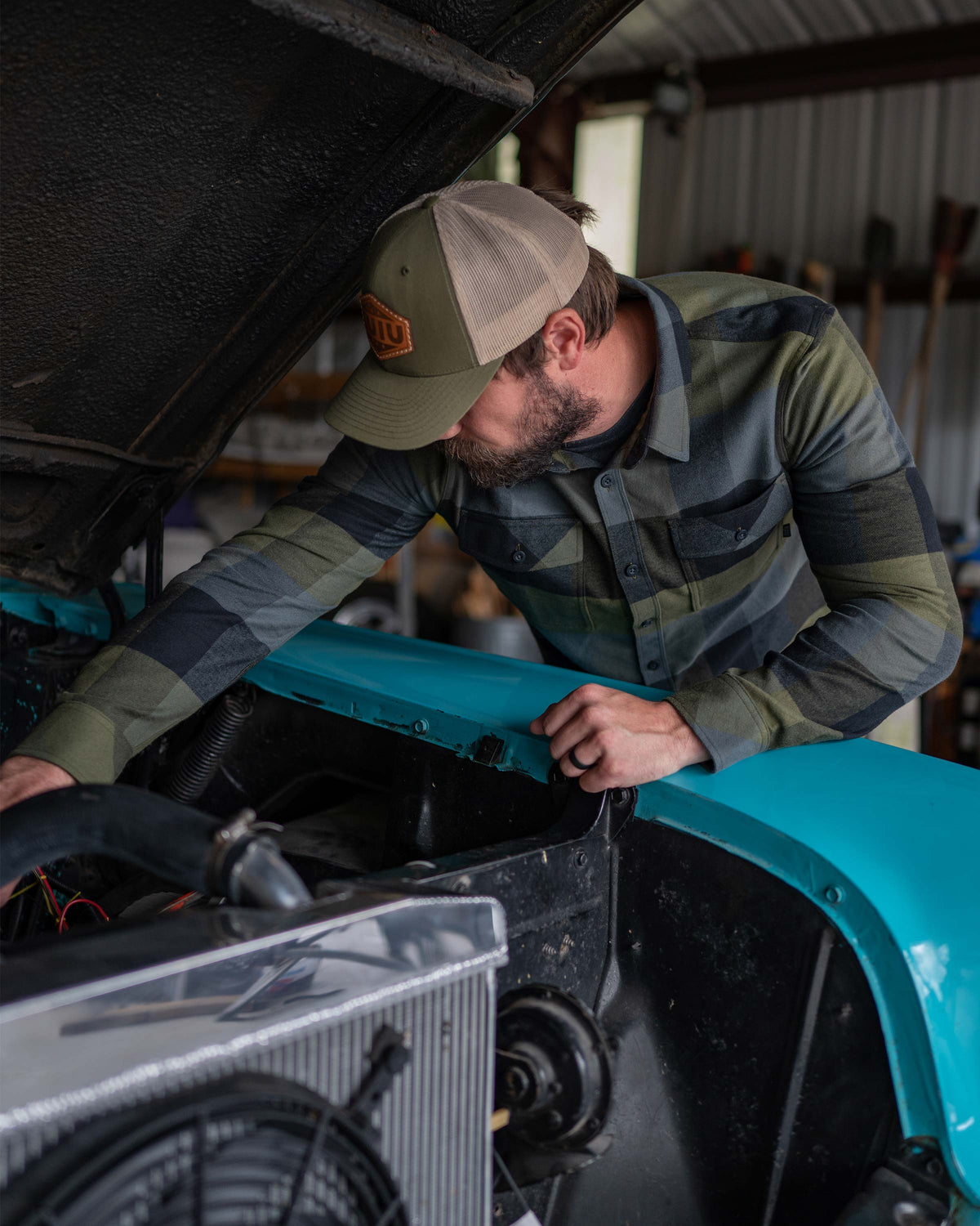 Man looking under a car hood, wearing Field Flannel Shirt in Verde Buffalo Check Plaid
