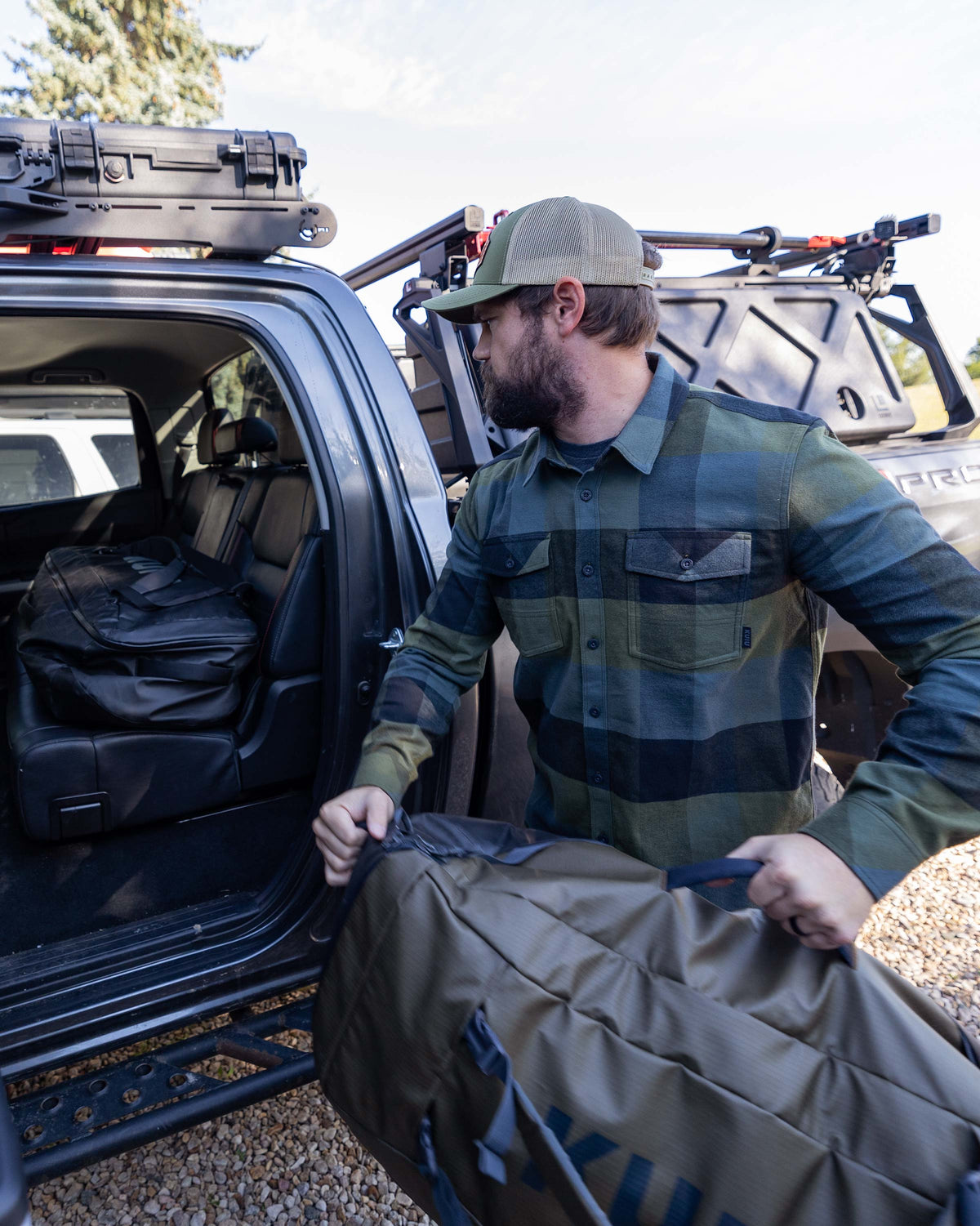 Hunter loading the Waypoint Duffel Bag into his vehicle, wearing Field Flannel Shirt in Verde Buffalo Check Plaid