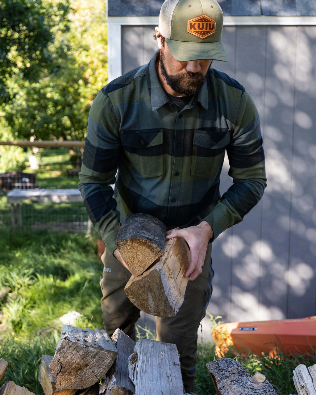 Hunter in an outdoor setting stacking firewood logs, wearing Field Flannel Shirt in Verde Buffalo Check Plaid