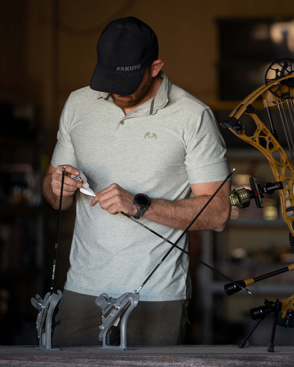 Hunter gluing the fletching on his arrow, wearing KUIU Performance Polo T-Shirt in Heather Buckbrush