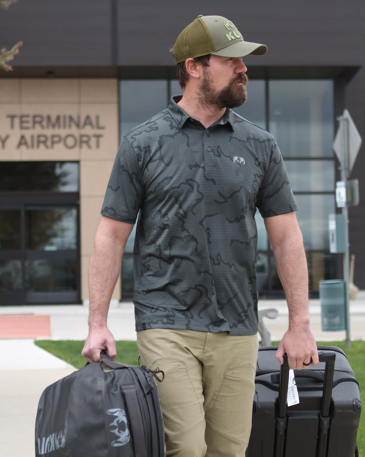 Hunter walking out of airport terminal with his luggages, wearing KUIU Perfomance Polo T-Shirt in Gunmetal Grey Tonal Print