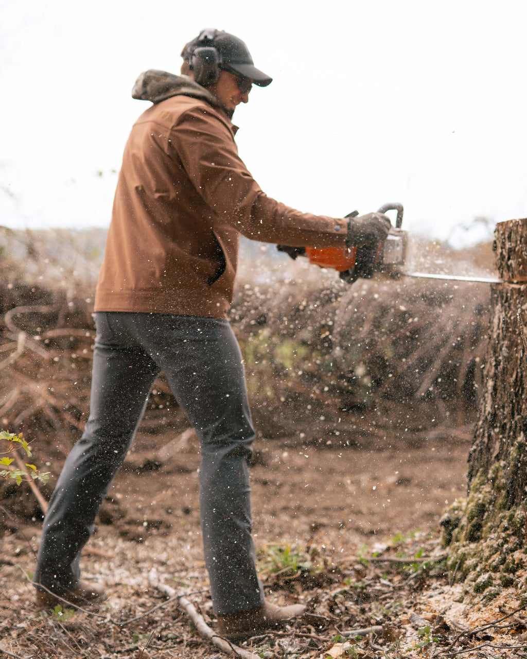 Man standing and sawing a tree trunk, wearing Brawley Jacket in Saddle Brown