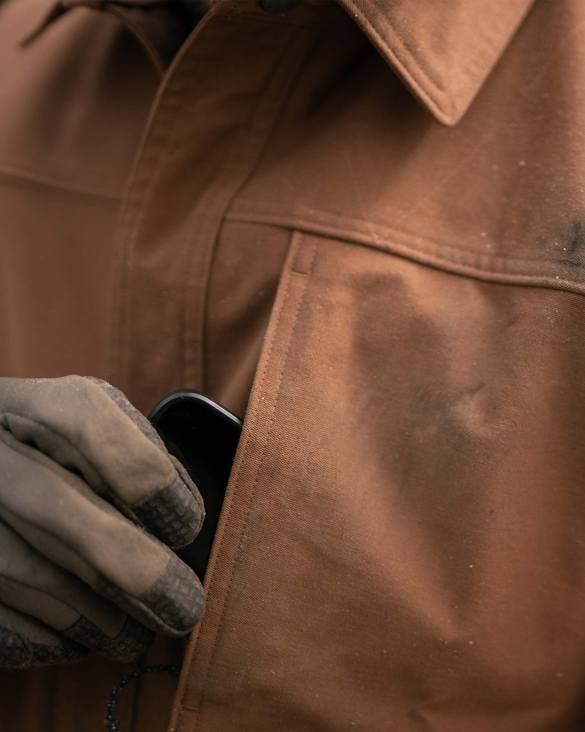 Up close view of man putting his cellphone in the left vertical chest pocket on Brawley Canvas Jacket in Saddle Brown