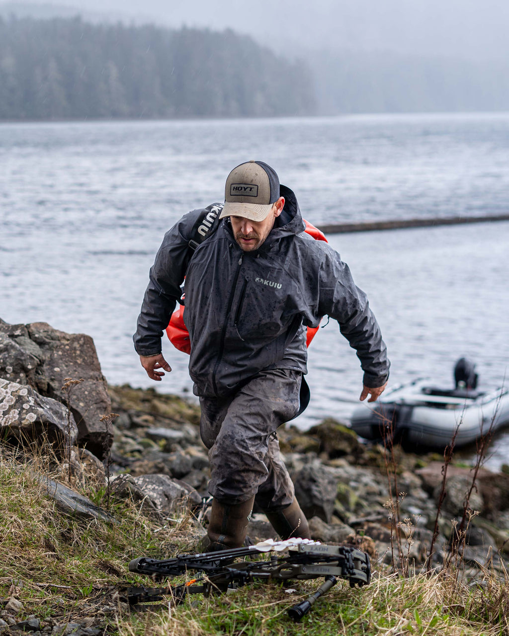 Hunter walking on land and away from his speed boat, wearing the Northridge Rain Pant and Jacket in Gunmetal Grey and carrying a Taku 5500 gear bag