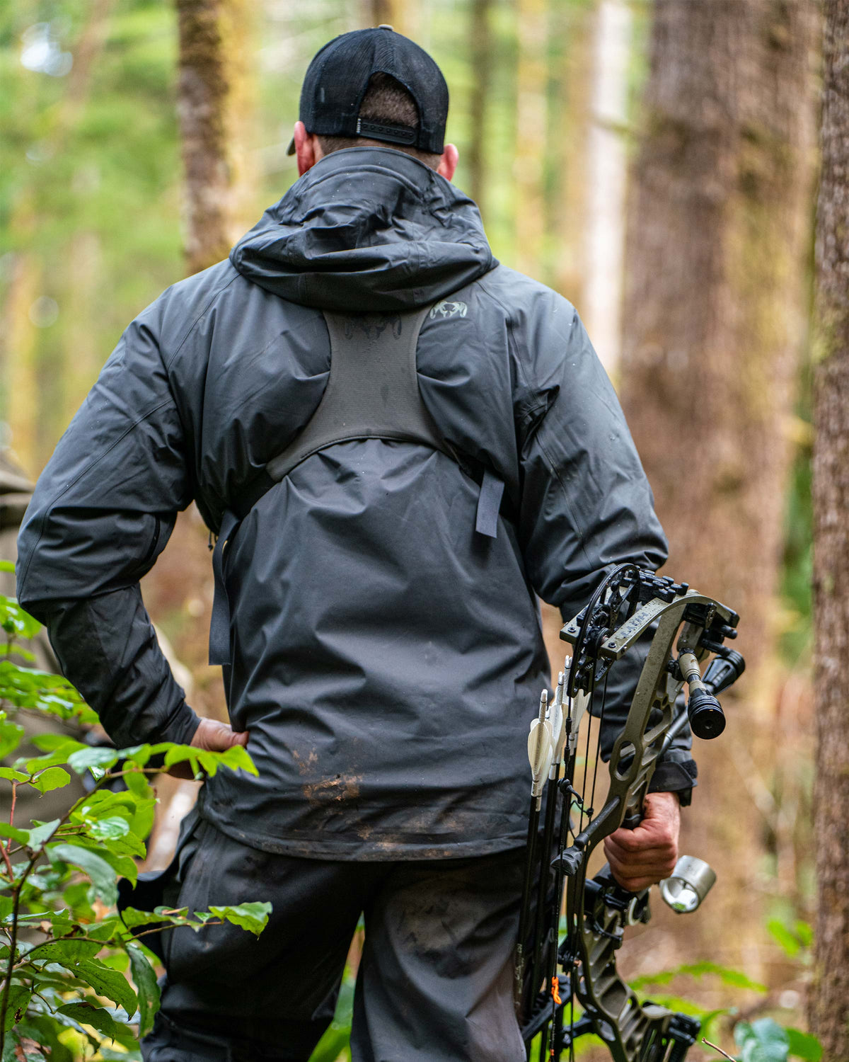 Back view of Hunter standing in the forest  carrying a bow, wearing Northridge Rain Jacket in Gunmetal Grey