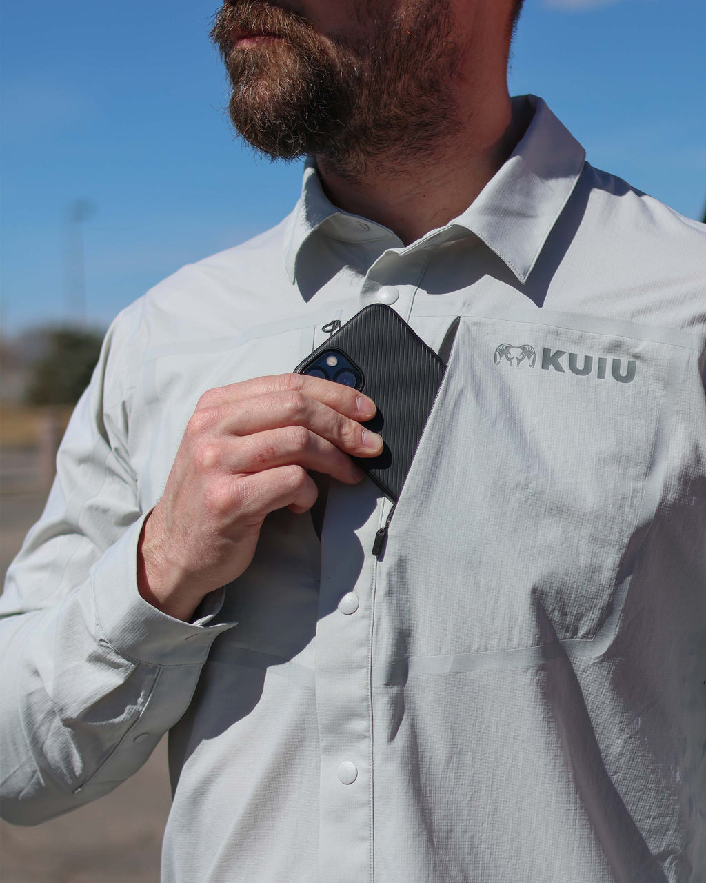 Man wearing Salton Long Sleeve Shirt in Lunar Grey, putting a cell phone in his front left chest pocket 