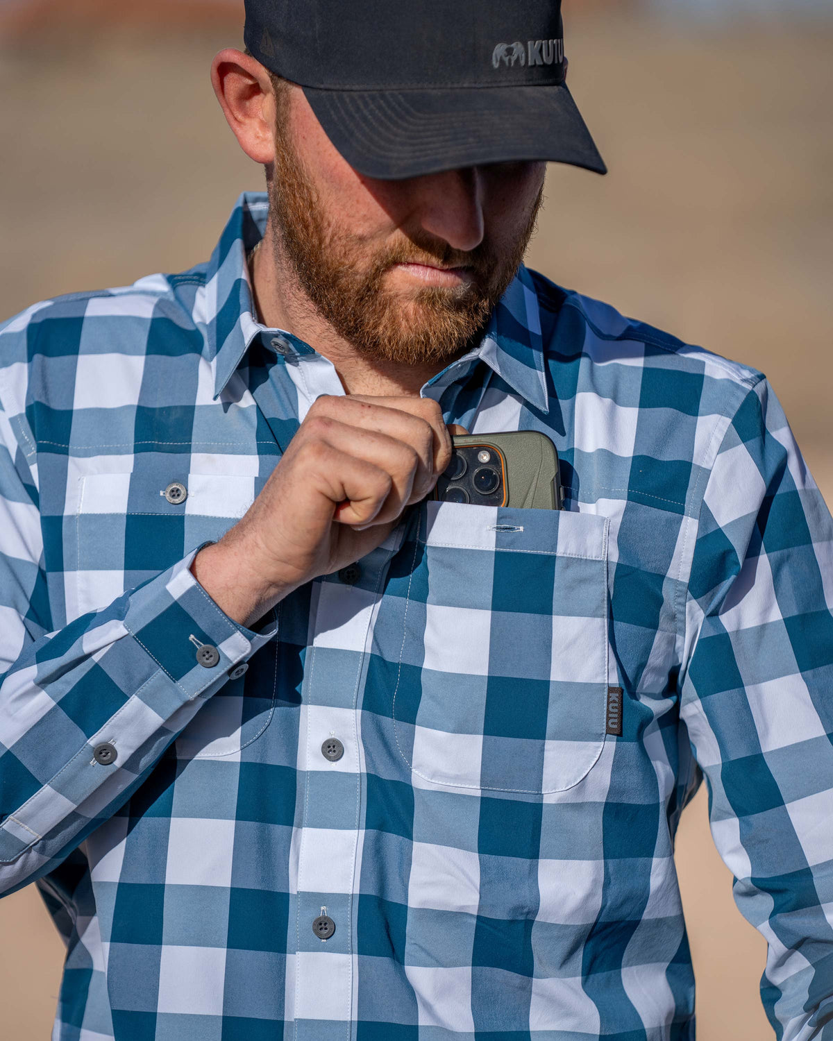 Hunter wearing Borrego LS Shirt in Blue Lake Plaid, putting a cell phone in his left chest pocket