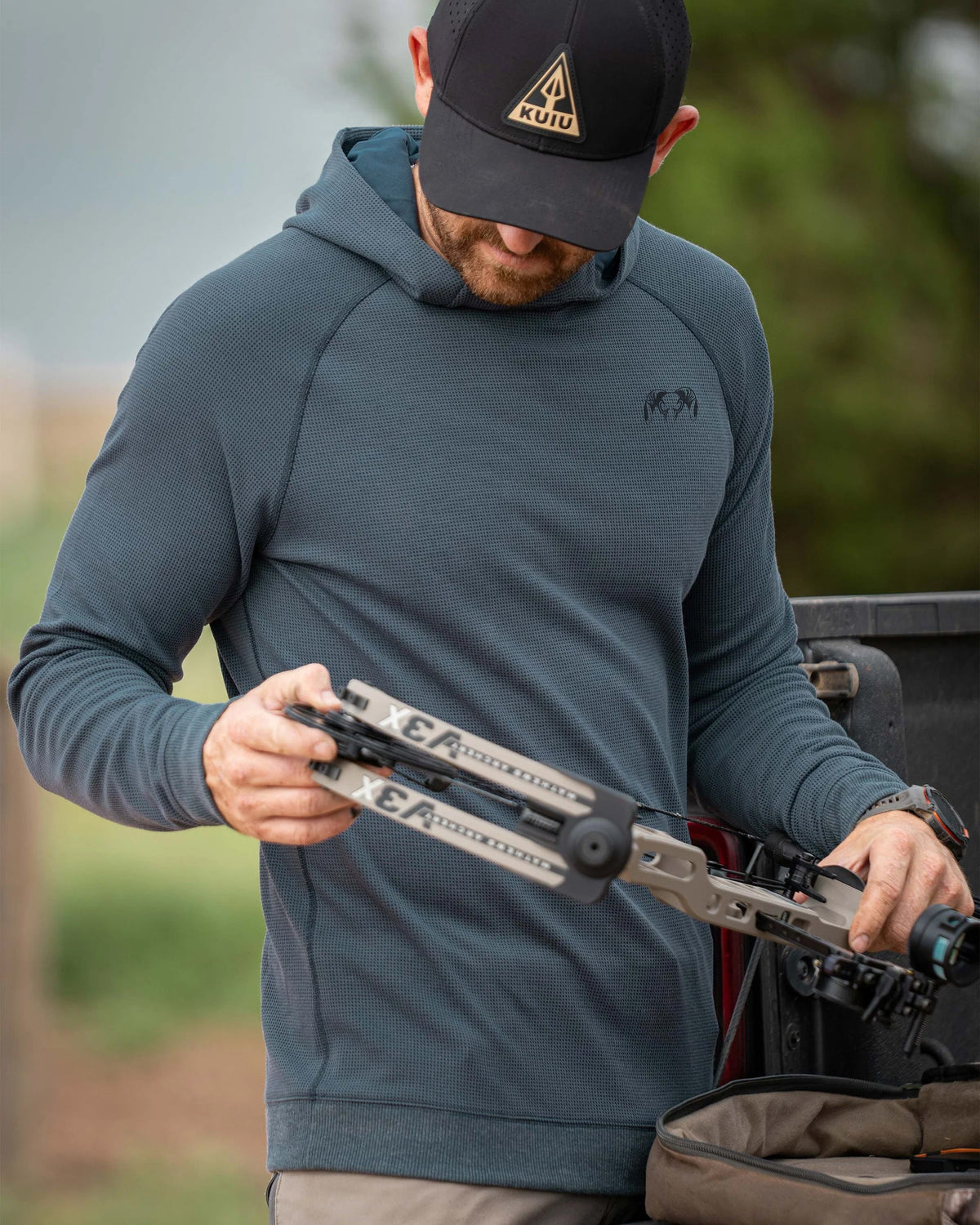 Man accesses his bow wearing Canyon Waffle Hoodie in Steel Blue