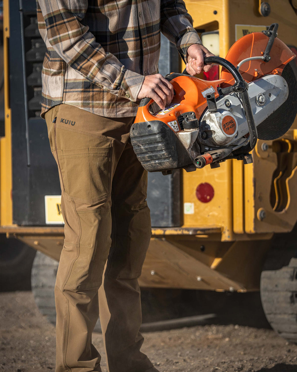 Man holding an orange and black STIHL‑branded cutoff saw, gripping it with both hands, Wearing Groundwork Stretch Woven Pant in Tobacco Brown
