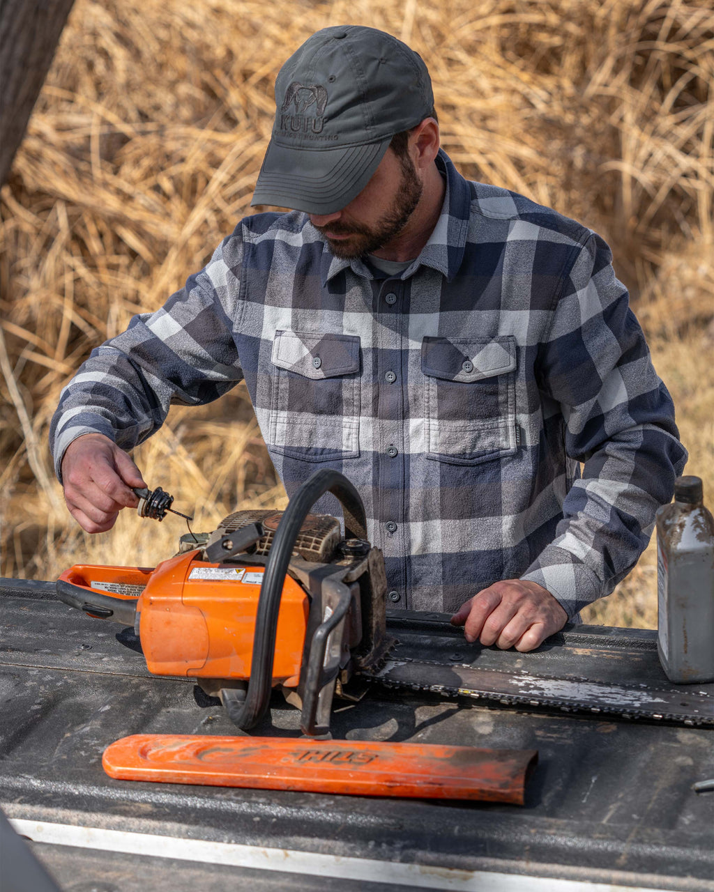 Hunter checking the oil level on his gas chainsaw, wearing Field Flannel Shirt in Steel Blue Trio