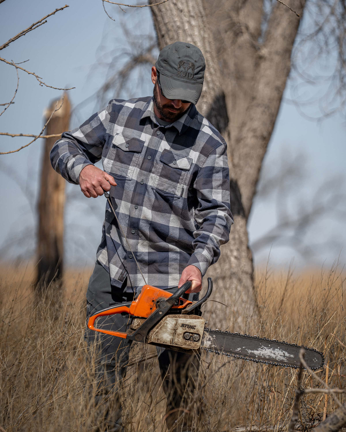Hunter in the field, pulling on the start cord on his chain saw, wearing Field Flannel Shirt in Steel Blue Trio