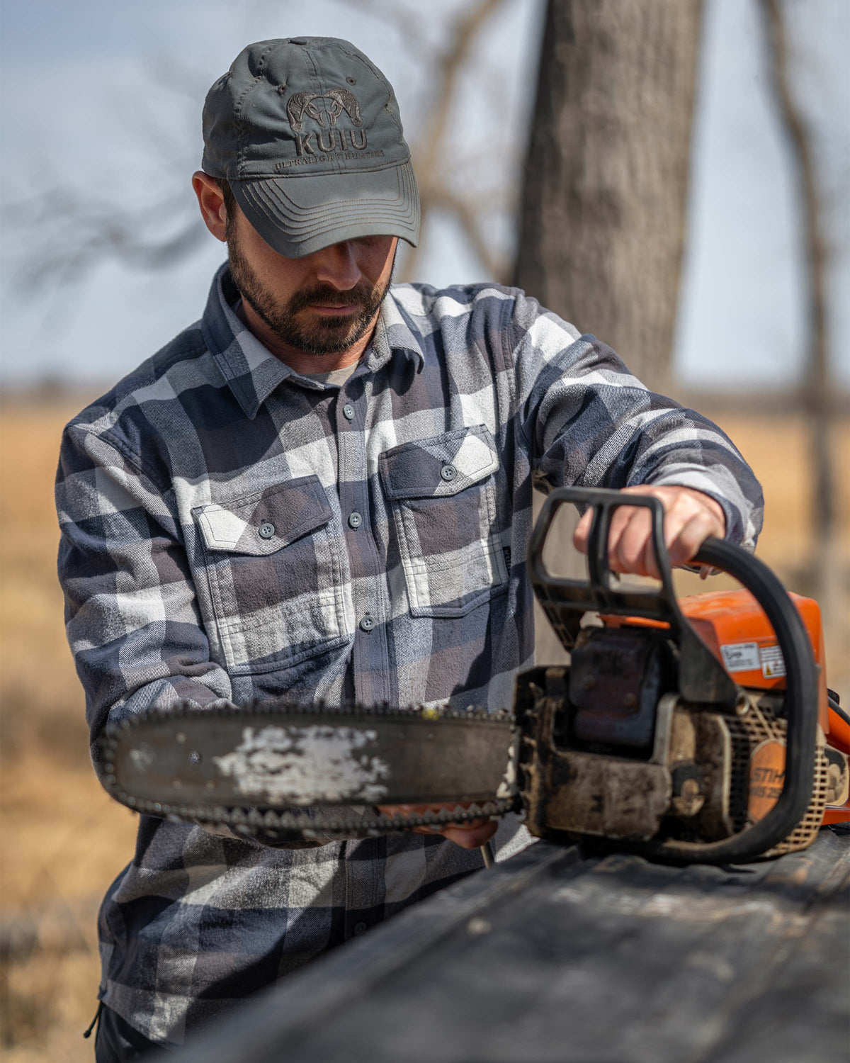 Hunter placing his chainsaw on the truck tailgate getting ready to use it, wearing Field Flannel in Steel Blue Trio