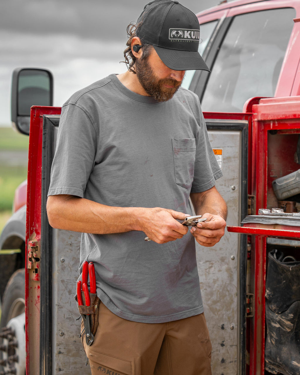 Man standing next to his truck with a built-in utility tool chest, holding a plier, wearing Workgrade Short Sleeve Pocket Crew T-Shirt in Castle Rock Grey