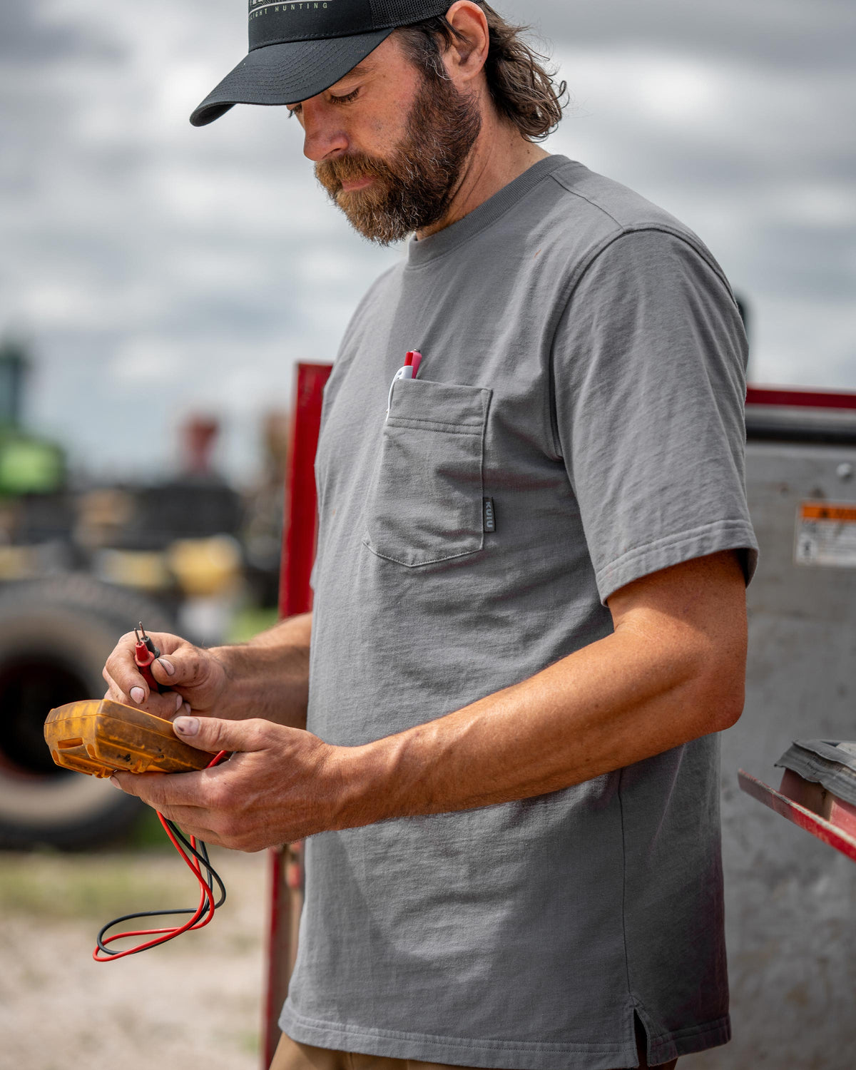 Man holding an electrical meter standing next to utility truck, wearing Workgrade Short Sleeve Pocket Crew 
