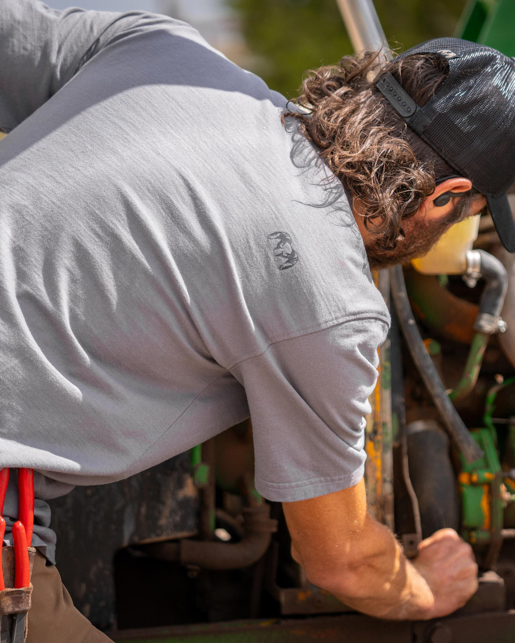 Back view of man slighting bent over looking at a truck engine wearing Workgrade Short Sleeve Pocket Crew in Castle Rock Grey, Highlighting right shoulder KUIU Ram Logo 