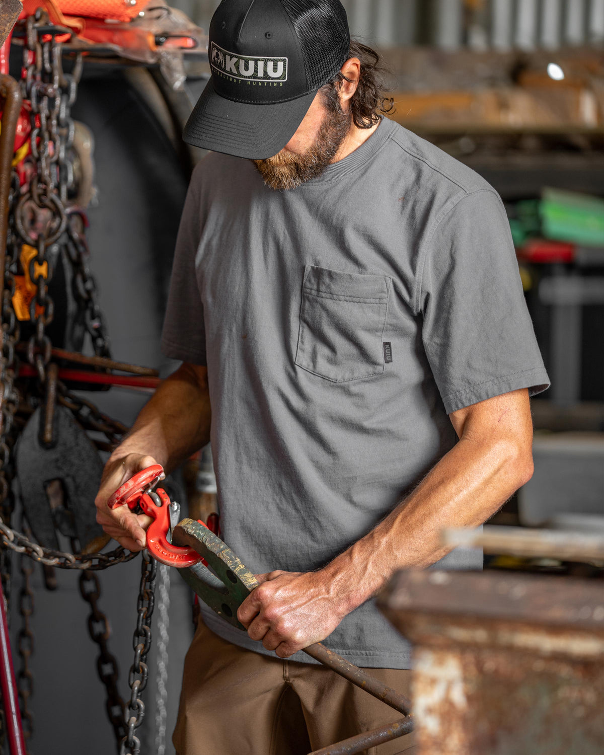 Man connecting chains in a workshop setting, wearing Workgrade Short Sleeve Pocket Crew in Castle Rock Grey
