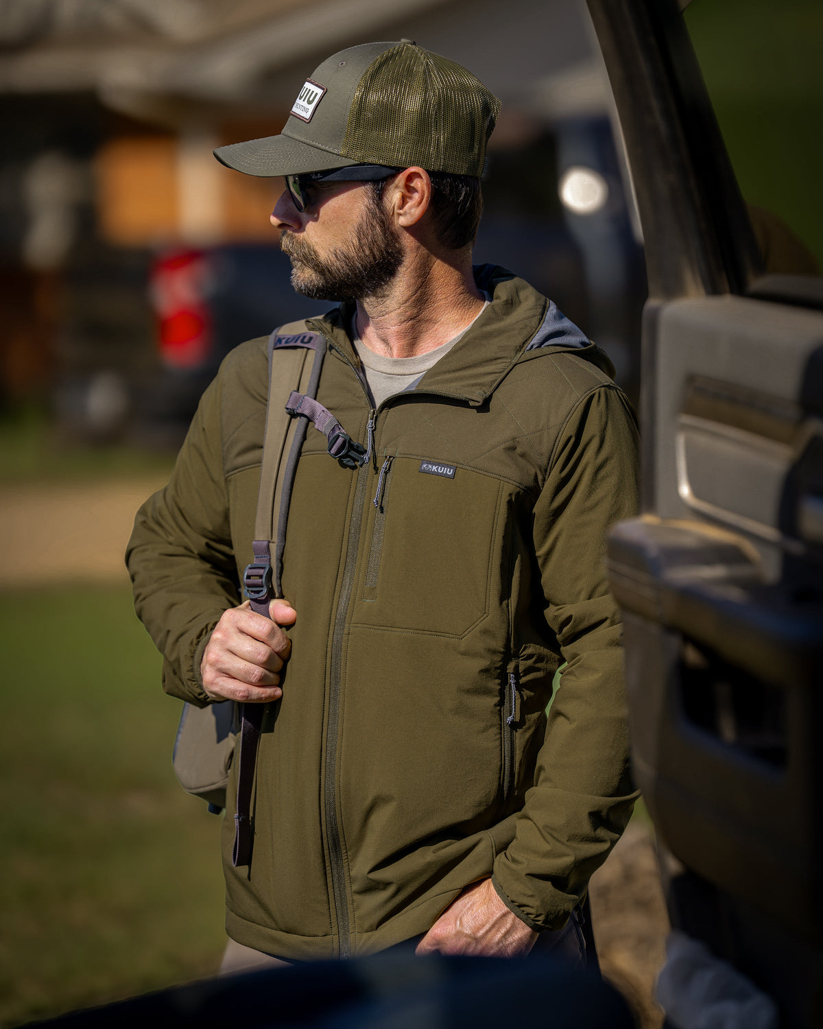 A man wearing a Transit Packable Hooded Jacket in Dark Army/Army Green, standing outdoors next to a vehicle.