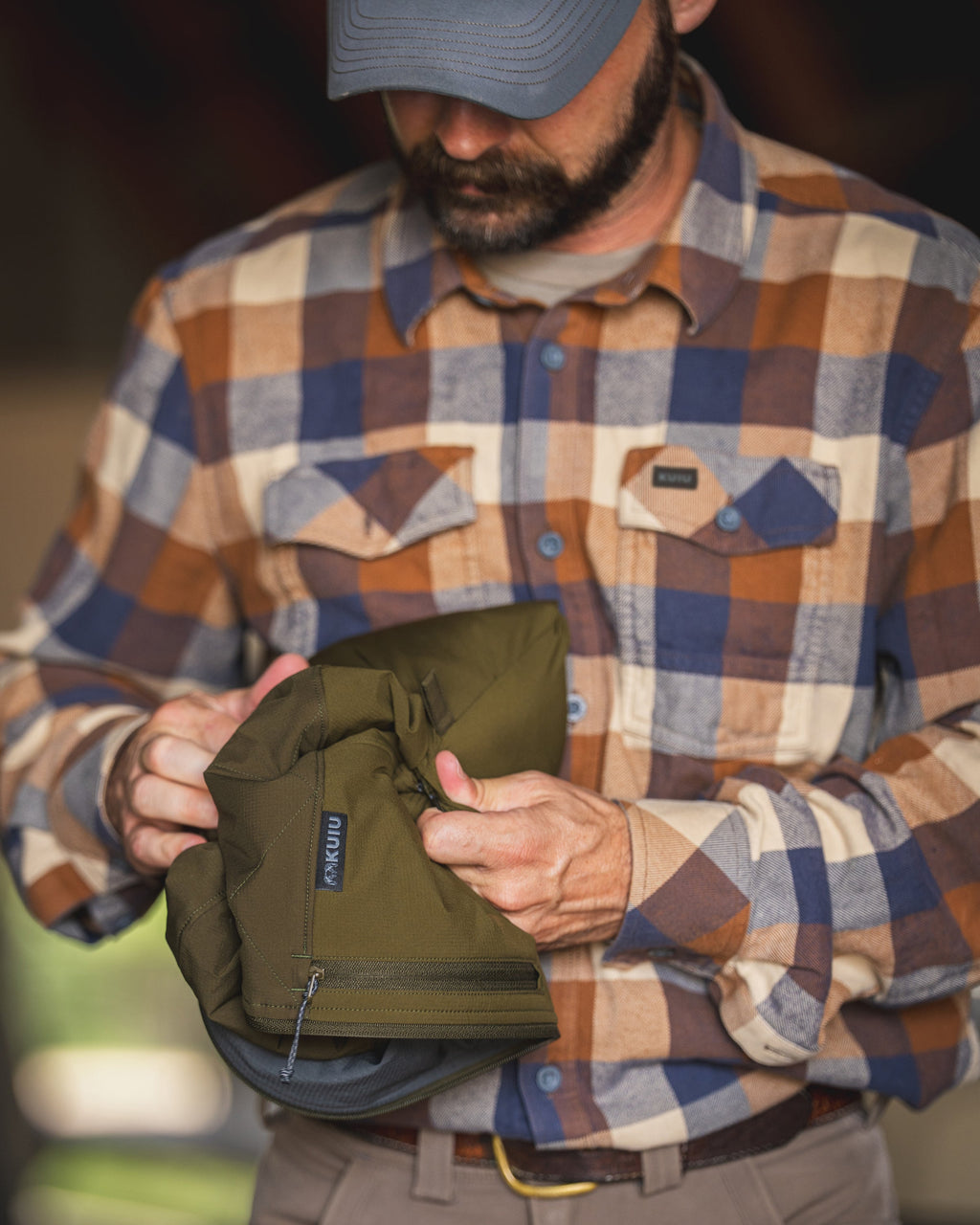 A man folding and showcasing a packable Transit Hooded Jacket in Dark Army/Army Green.
