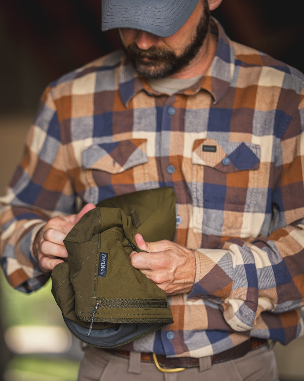 A man folding and showcasing a packable Transit Hooded Jacket in Dark Army/Army Green.