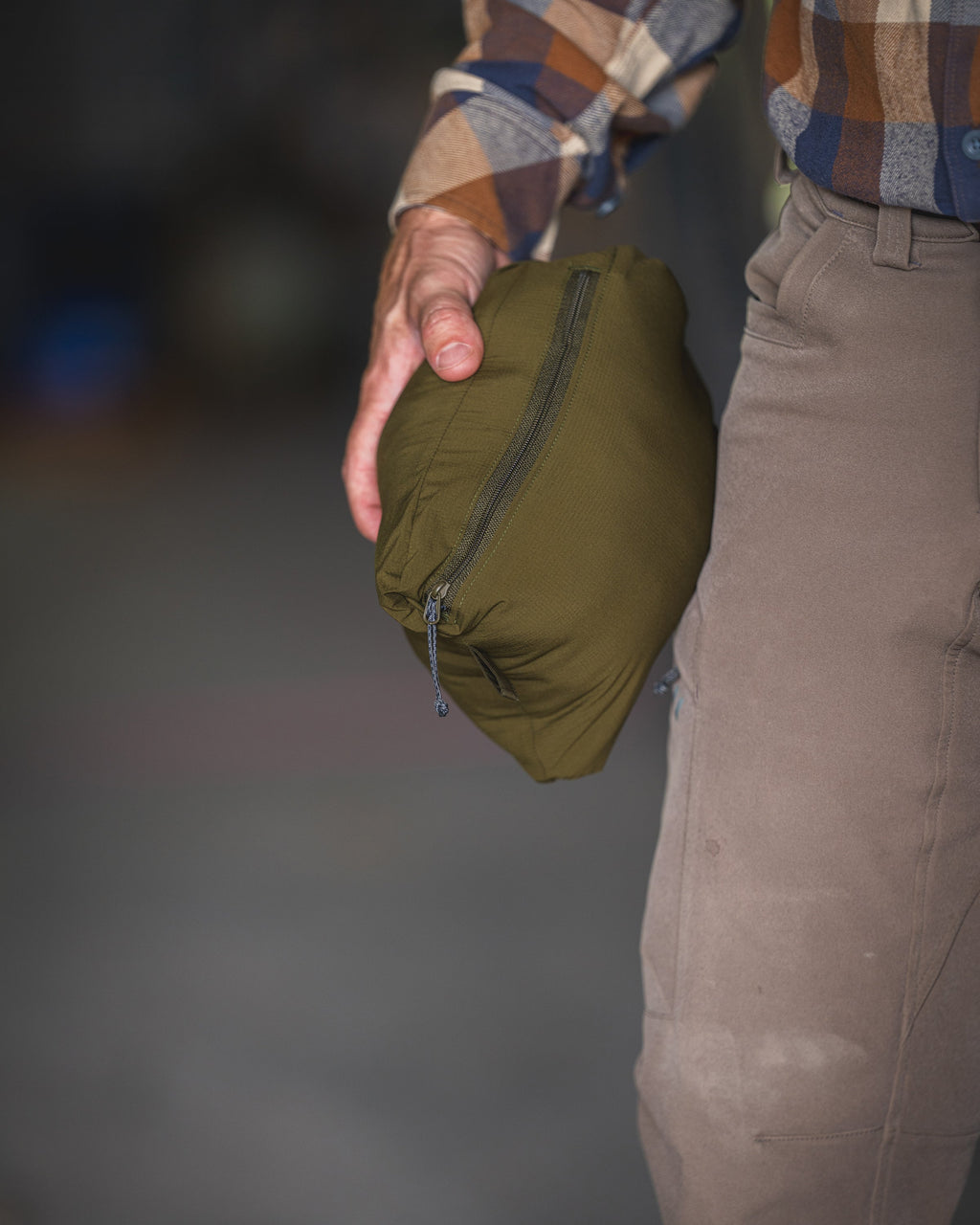 Close-up view of a person holding a self-stow, packable Transit Hooded Jacket in Dark Army/Army Green.