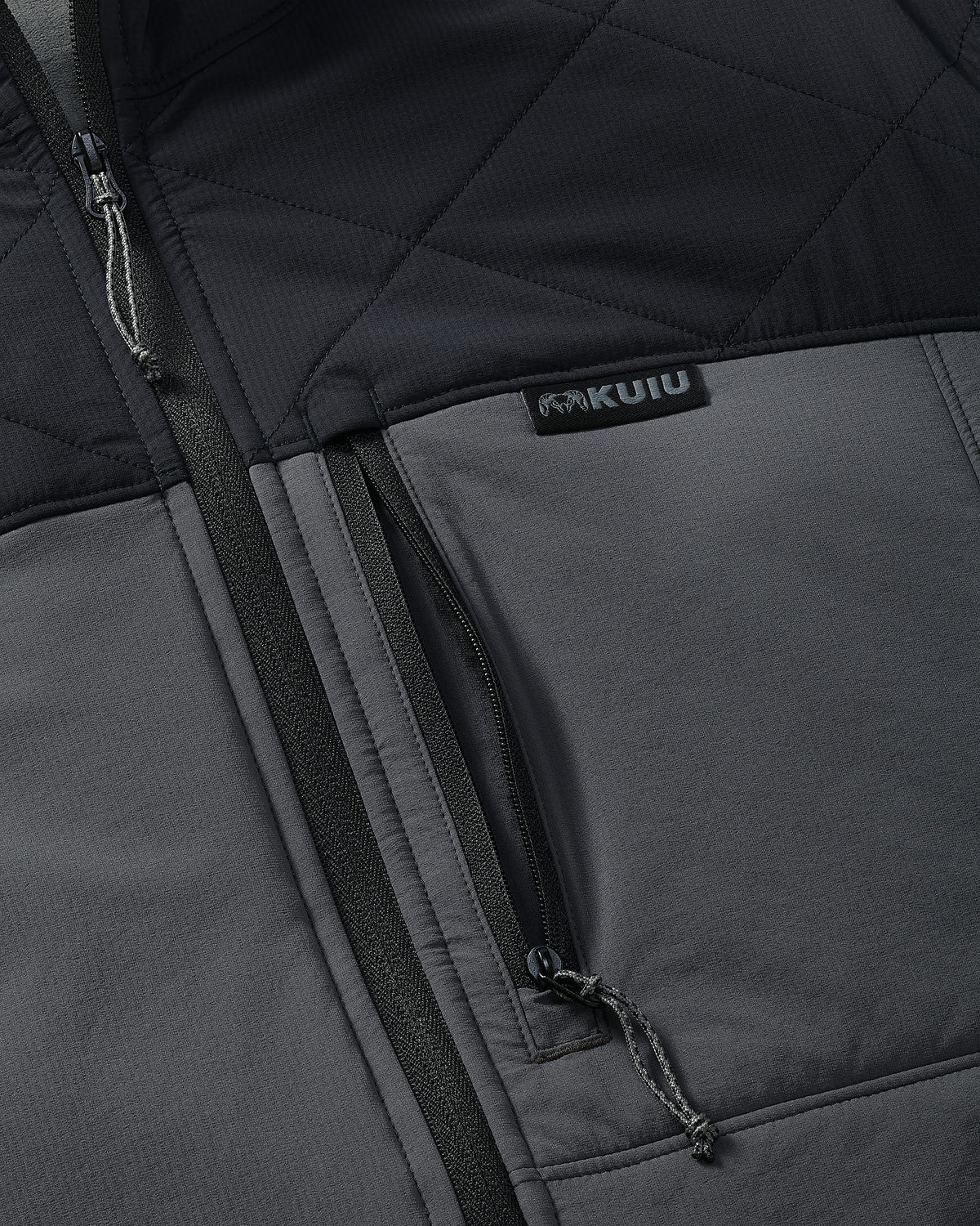 Close-up of an Transit Packable Hooded Jacket in Black/Gunmetal with a vertical zippered pocket and a visible KUIU brand sewn-in label.