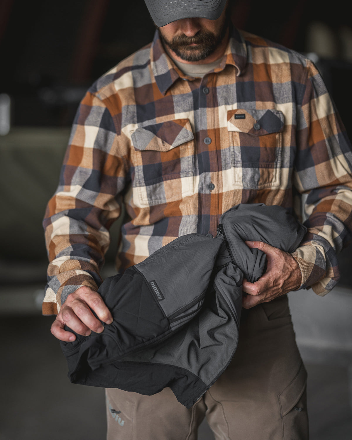 A man displaying folded Transit Packable Vest in Gunmetal in its self-stowing right-hand pocket.
