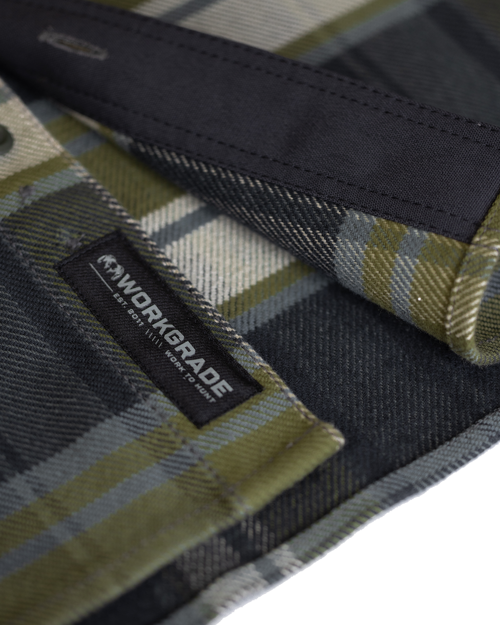 Close-up detail of durable stitching and texture of the fabric along the bottom corner heam, highlighting the sewn-in KUIU Workgrade label on the Flannel Heavyweight Shirt in Verde Check Plaid