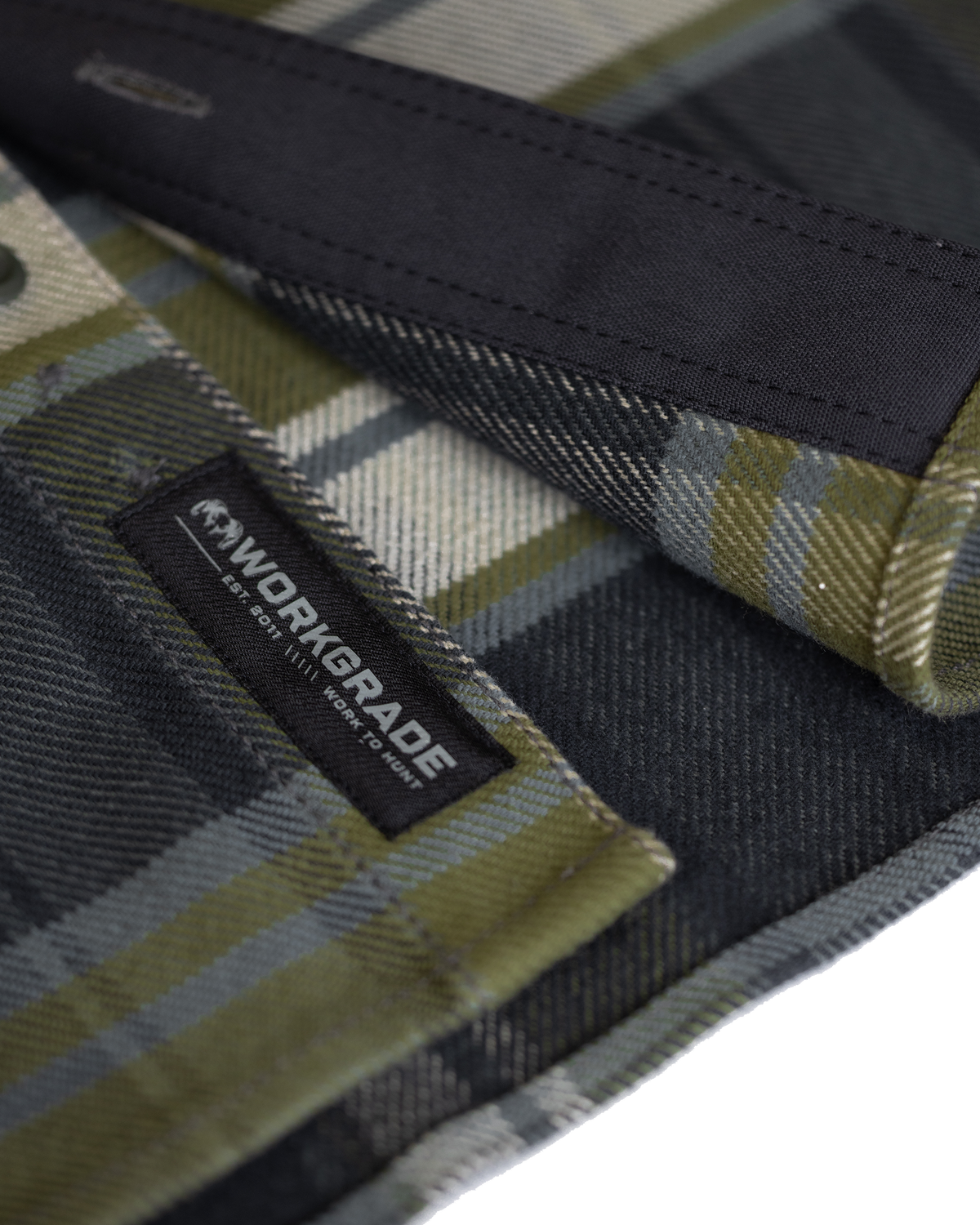 Close-up detail of durable stitching and texture of the fabric along the bottom corner heam, highlighting the sewn-in KUIU Workgrade label on the Flannel Heavyweight Shirt in Verde Check Plaid