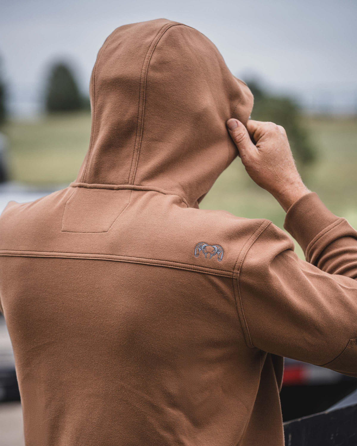Back view of a man pulling up the hood on a Workgrade Utility Hoodie in Saddle Brown 

