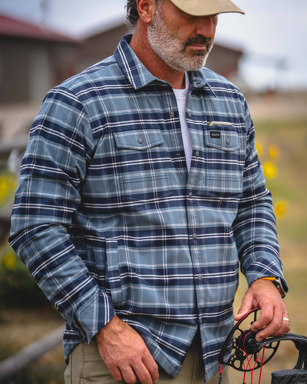 A man wearing KUIU Field Flannel Fleece in Steel Blue Framework, standing outdoors and holding a spool of fishing line.