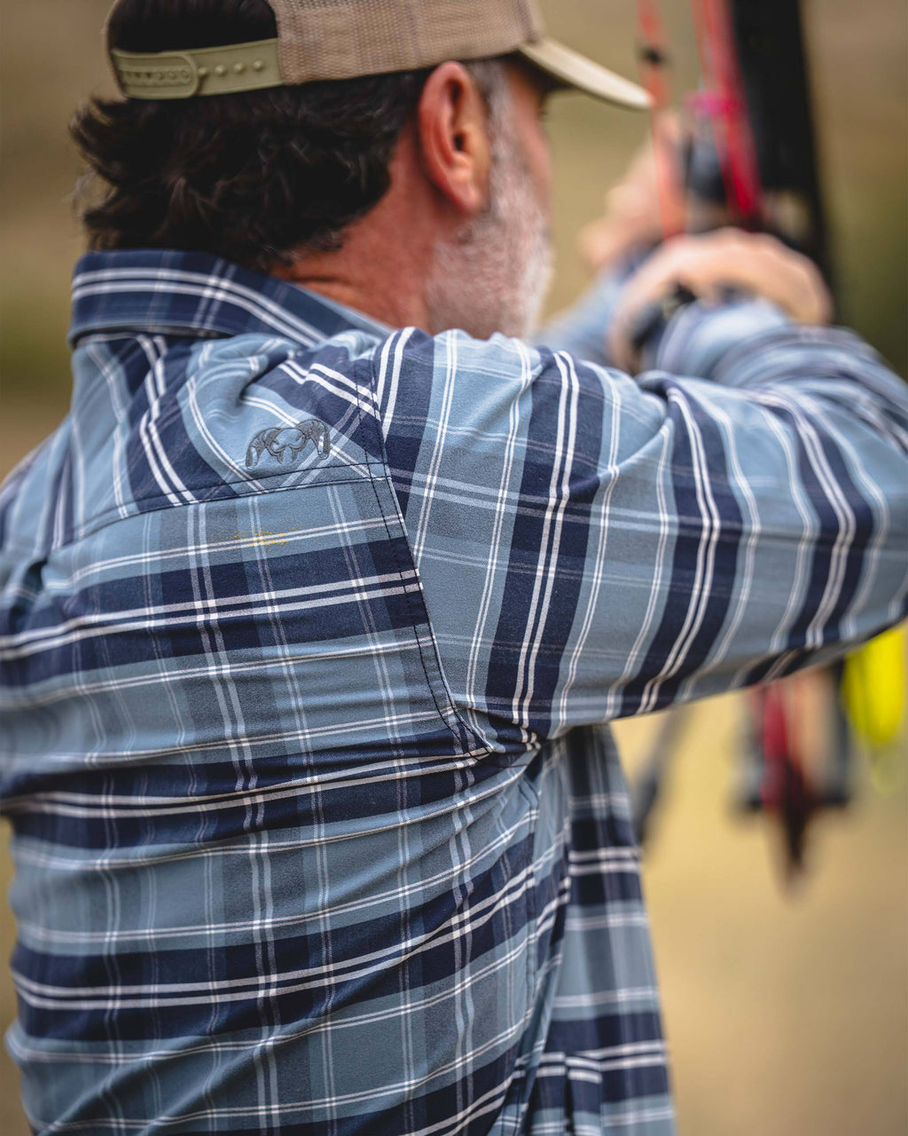 Back view of a man wearing KUIU Field Flannel Fleece in Steel Blue Framework, aiming a bow. 