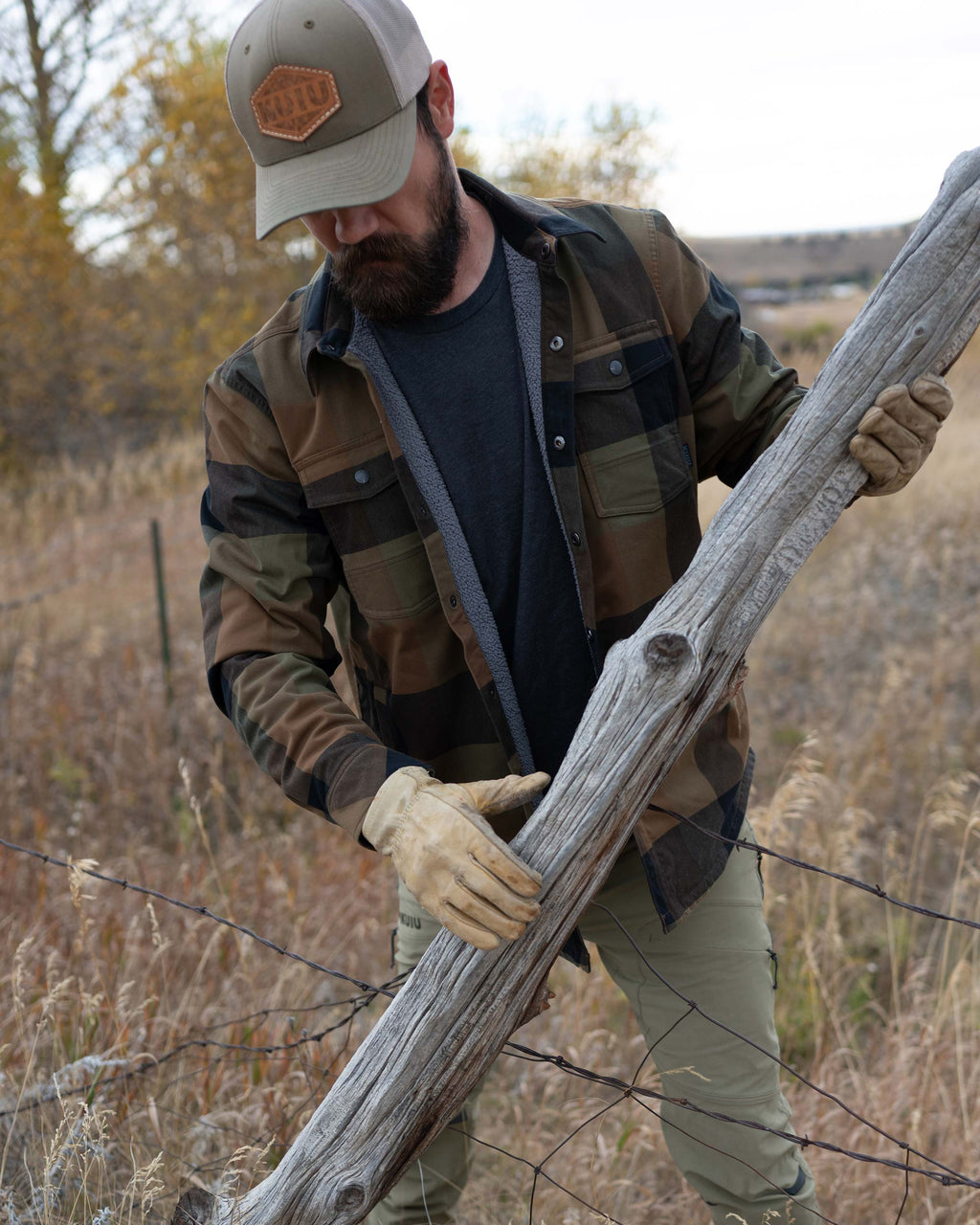 Hunter lifting a log over the wired fence, wearing Field Flannel Shirt Jacket in Valo Plaid